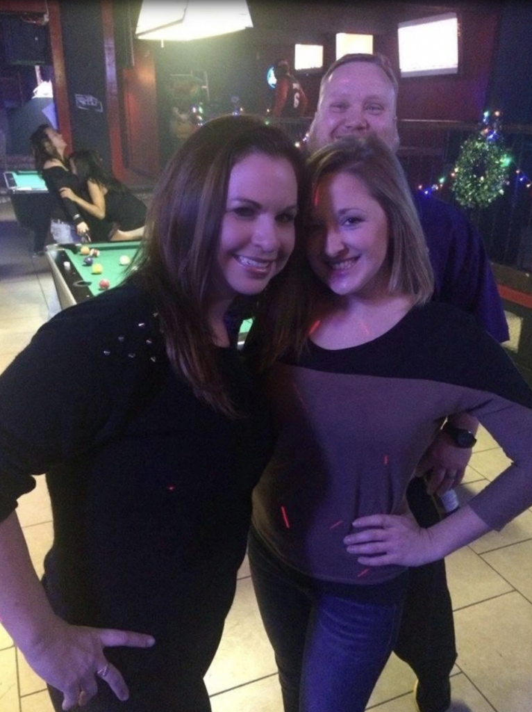 Image of two women smiling for photo, husband behind them, and then two women having a hug behind the pool table behind the. 