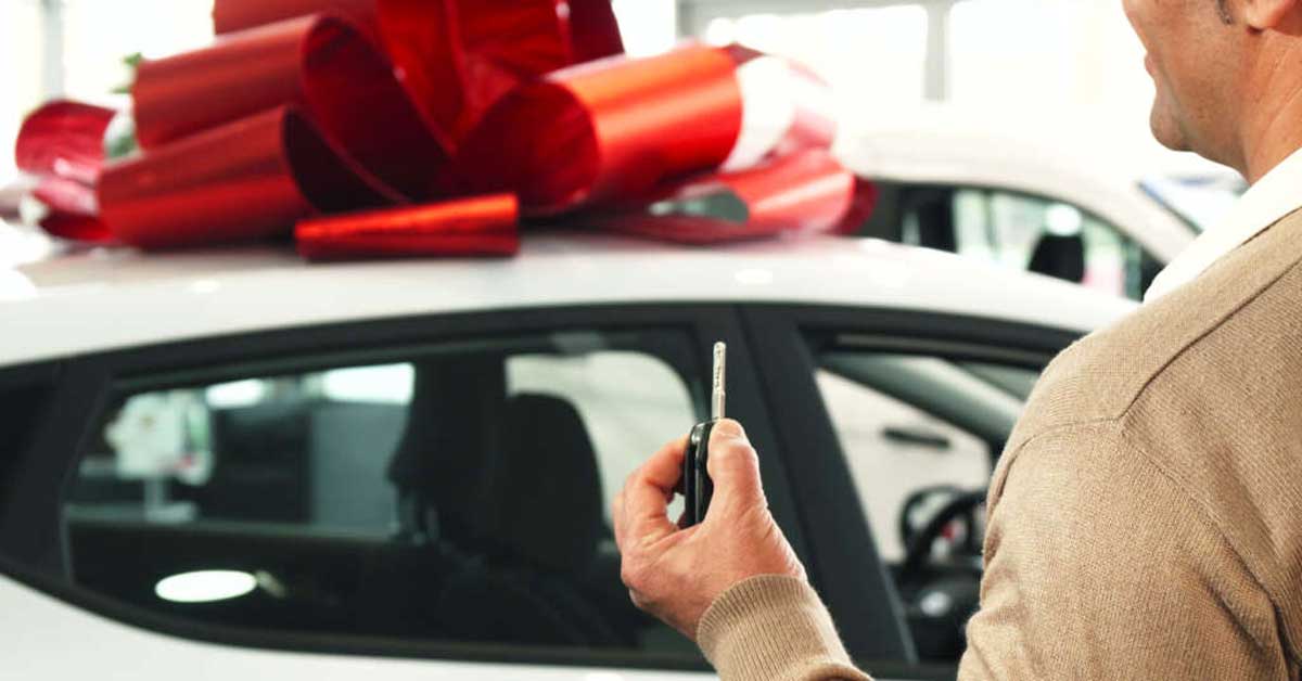 Guy holding car key in front of new car with a bow on it