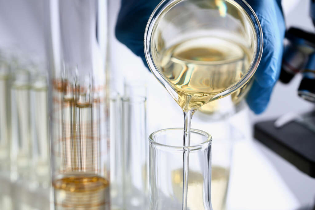 A close up image of a gloved hand pouring out a clear liquid. 