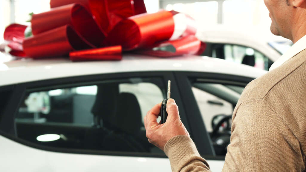 Man standing in front of a new car with a present bow and tie on it. 