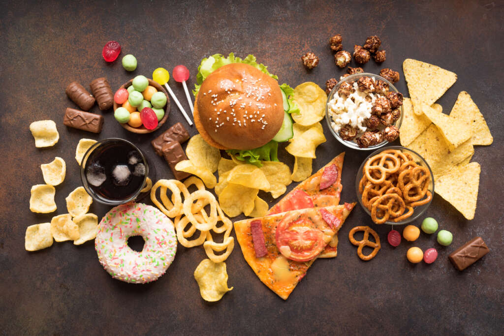 Different kinds of junk food including a burger, pizza slices, a donut, that have been spread out on a countertop. 