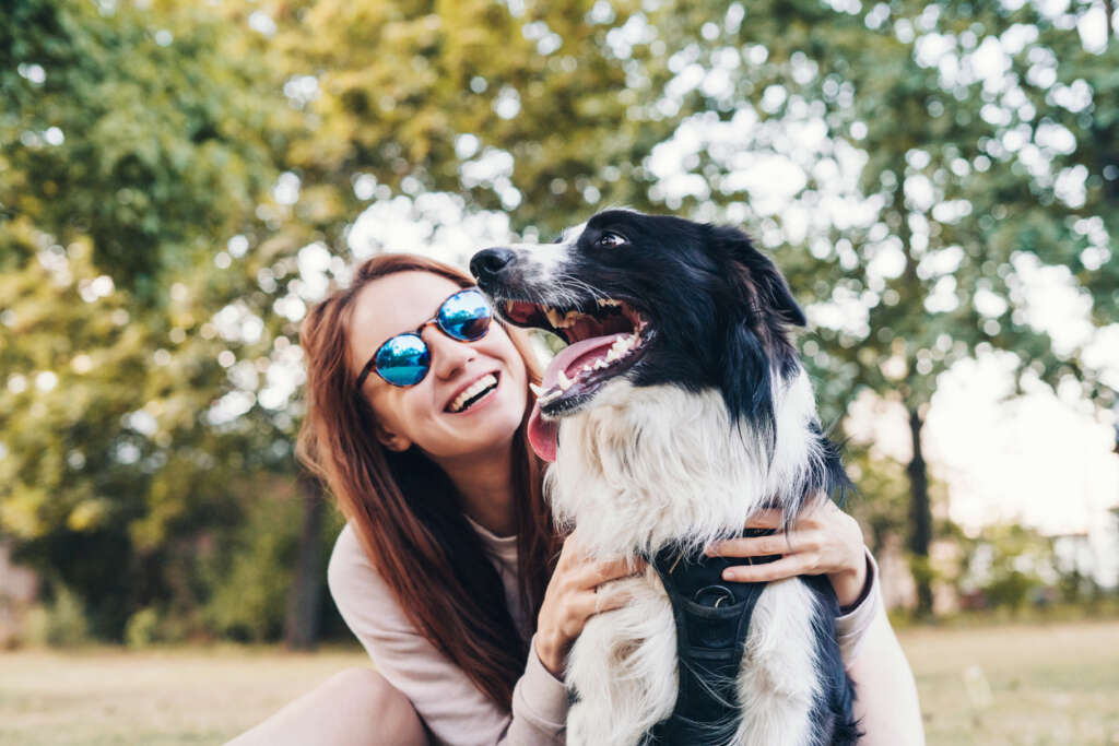 Woman smiling while looking at her dog on a sunny day in the park. 