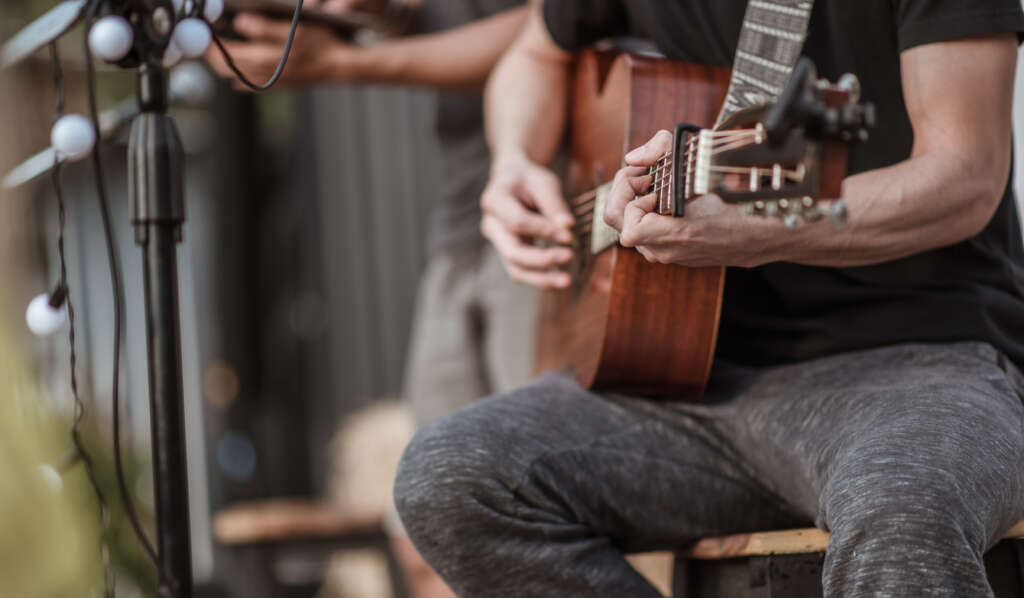 A man in a black shirt sitting on a music stage playing his guitar. 