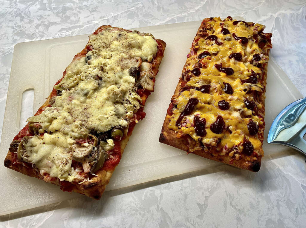Two different oven square pizzas that have been positioned next to each other on a cutting board. 