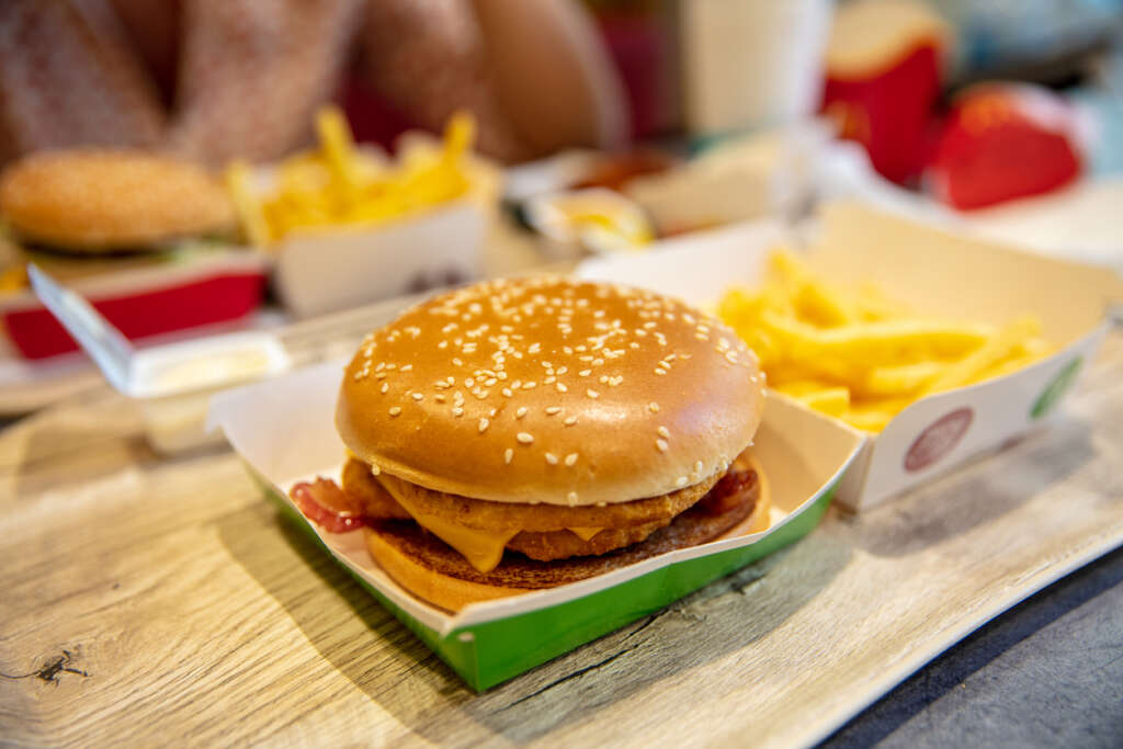 Close-up image of a fast food burger in its box next to french fries. 