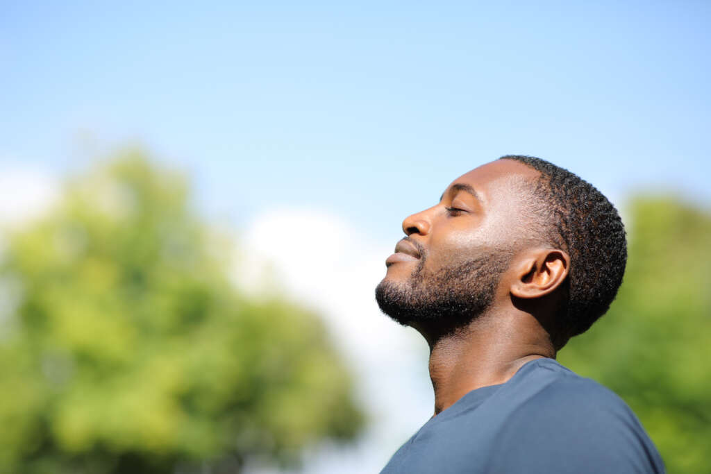 Man with his eyes closed, smiling, on a blue sky sunny day. 