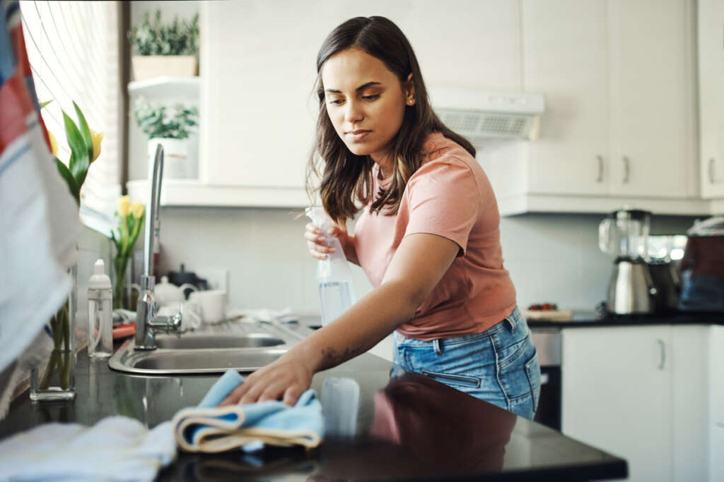 A woman using a dish rag while cleaning up the counter in her sink. 