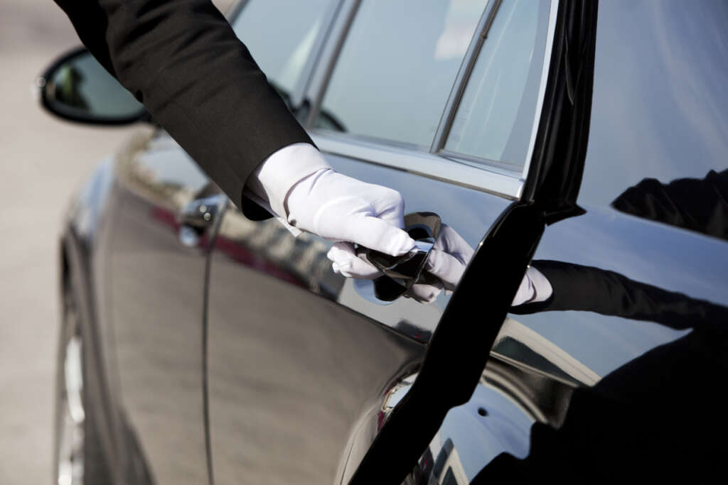 Image of a personal driver opening up their back door with their white glove on. 