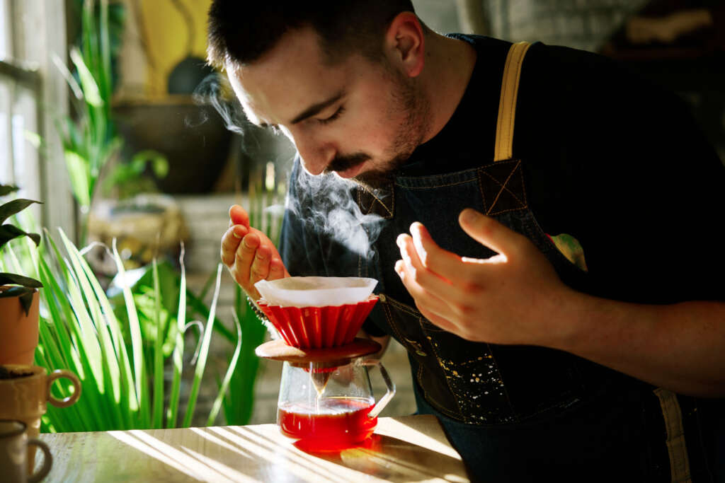 A close-up image of a young man smelling a coffee. 