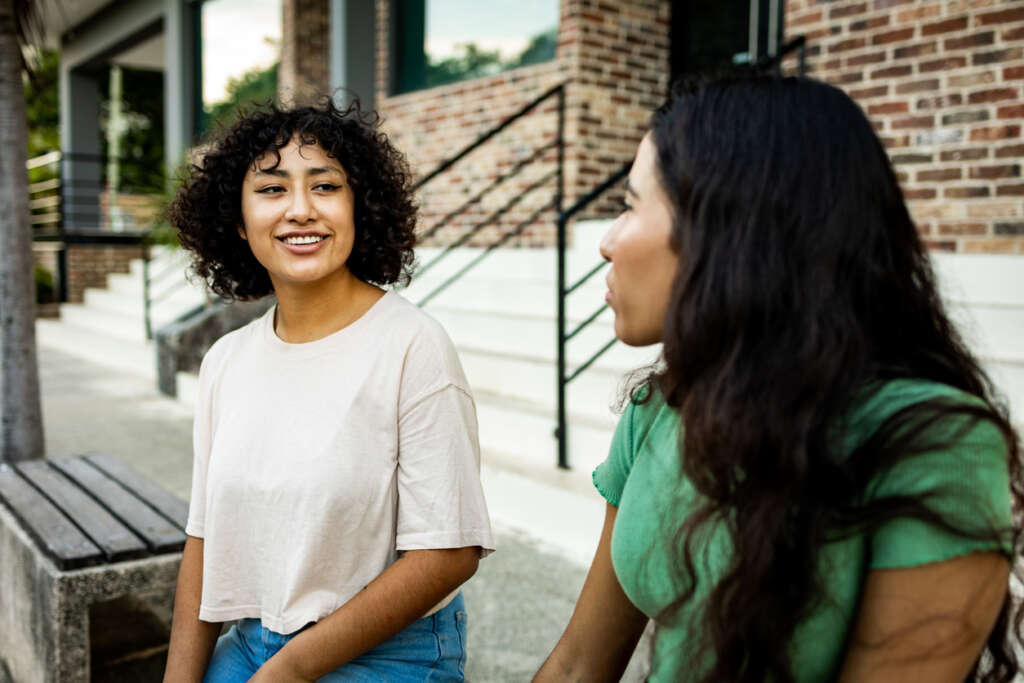 Two women having a conversation with one another, while one smiles after saying something. 