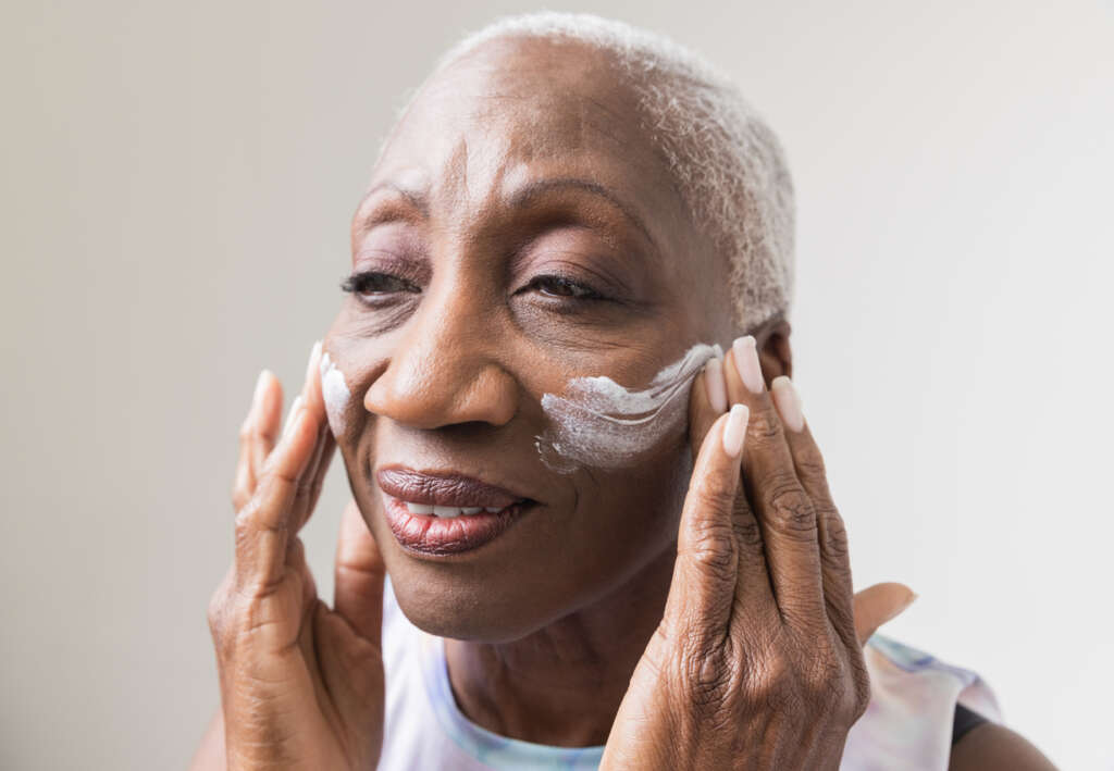 An older woman applying lotion to her face. 