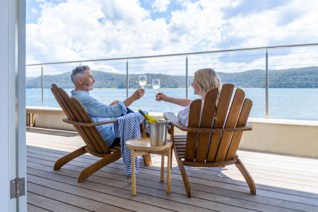 Image of a happy looking couple raising their glasses of wine while they have a nice view of the ocean. 