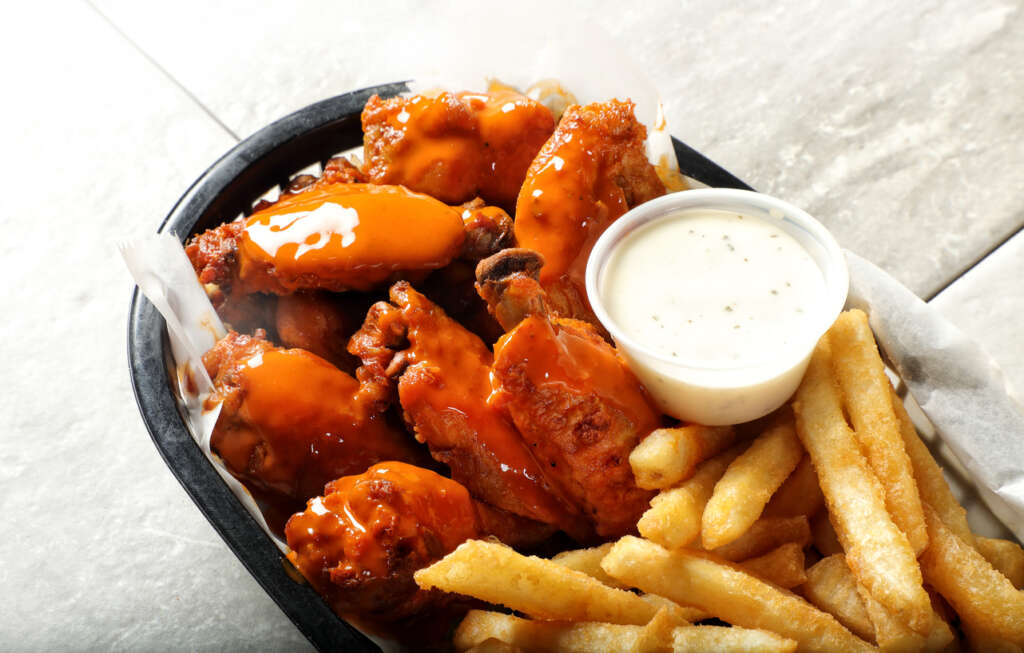 A close-up image of wings next to french fries. 