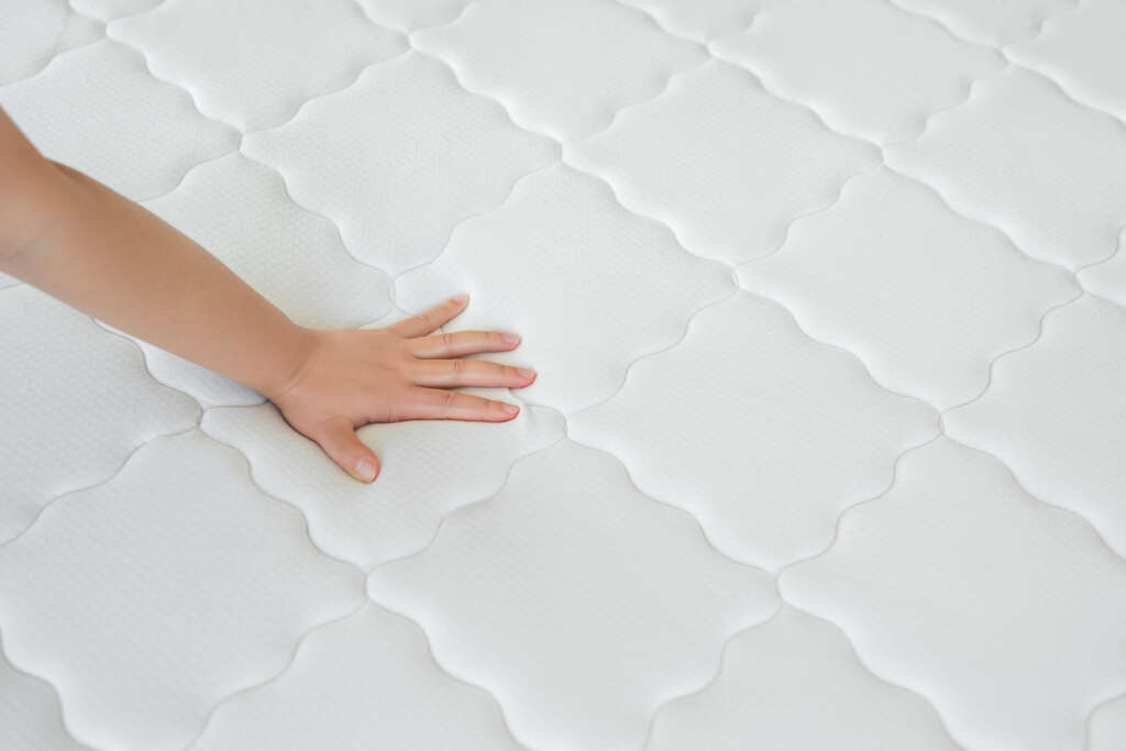 Image of a hand touching what looks like a very soft and new white mattress. 