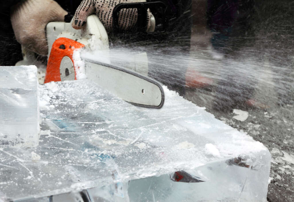 A close-up image of a chainsaw cutting through a giant block of ice. 