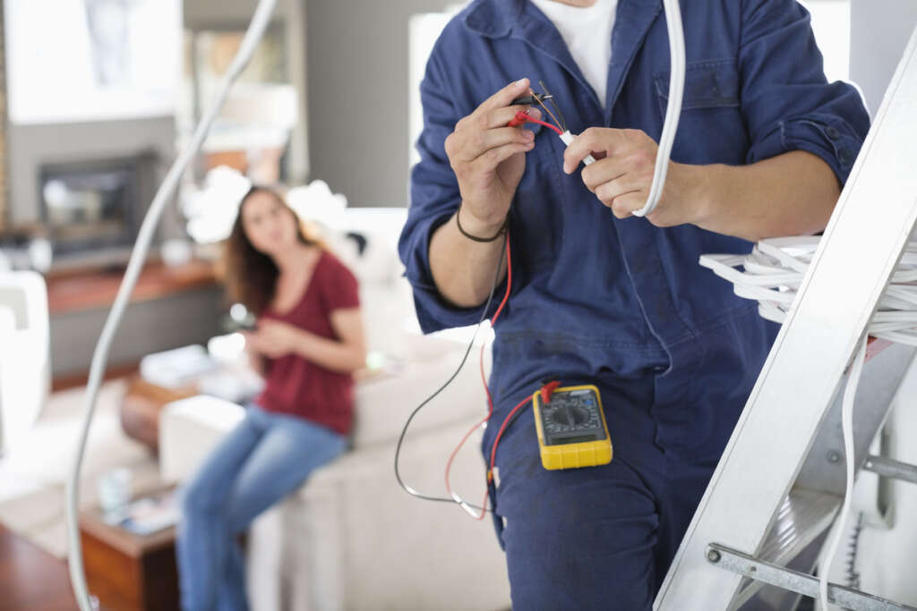 Image of a woman in her home's kitchen watching an electrician work on fixing a wire. 