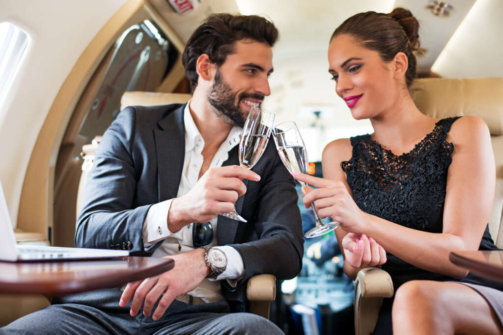 Image of a young couple cheers-ing their glasses of champagne while they are on board a private flight. 