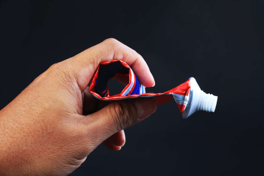 Hand holding a rolled up and emptied out toothpaste container. 