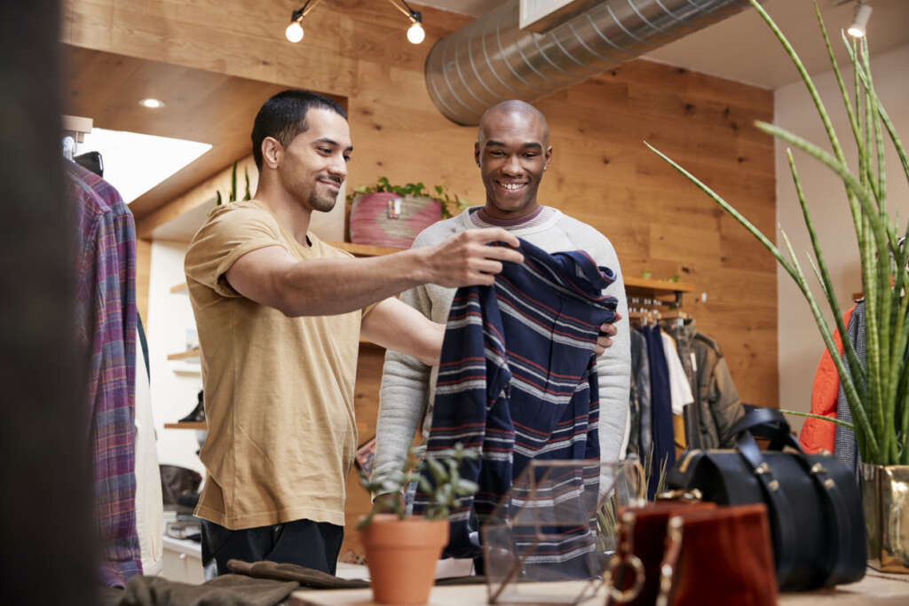 Image of a smiling man looking at a nice shirt while he shops around the store. 