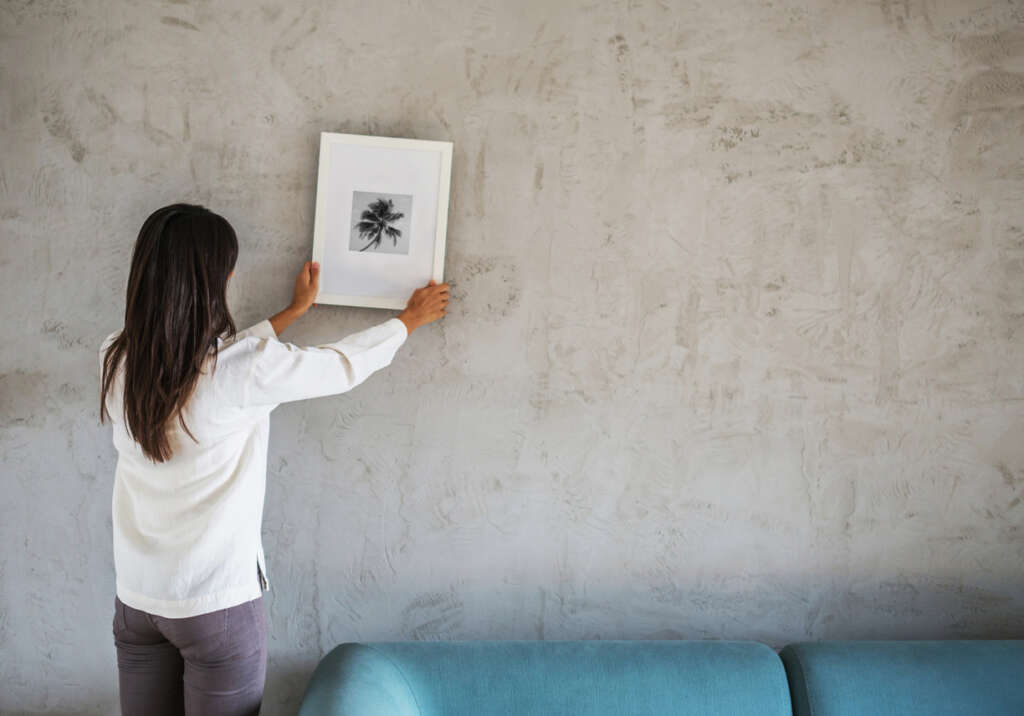 A woman hanging up a nice picture on a blank wall. 