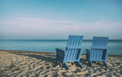 An image of two blue-colored beach chairs sitting in front of an ocean.