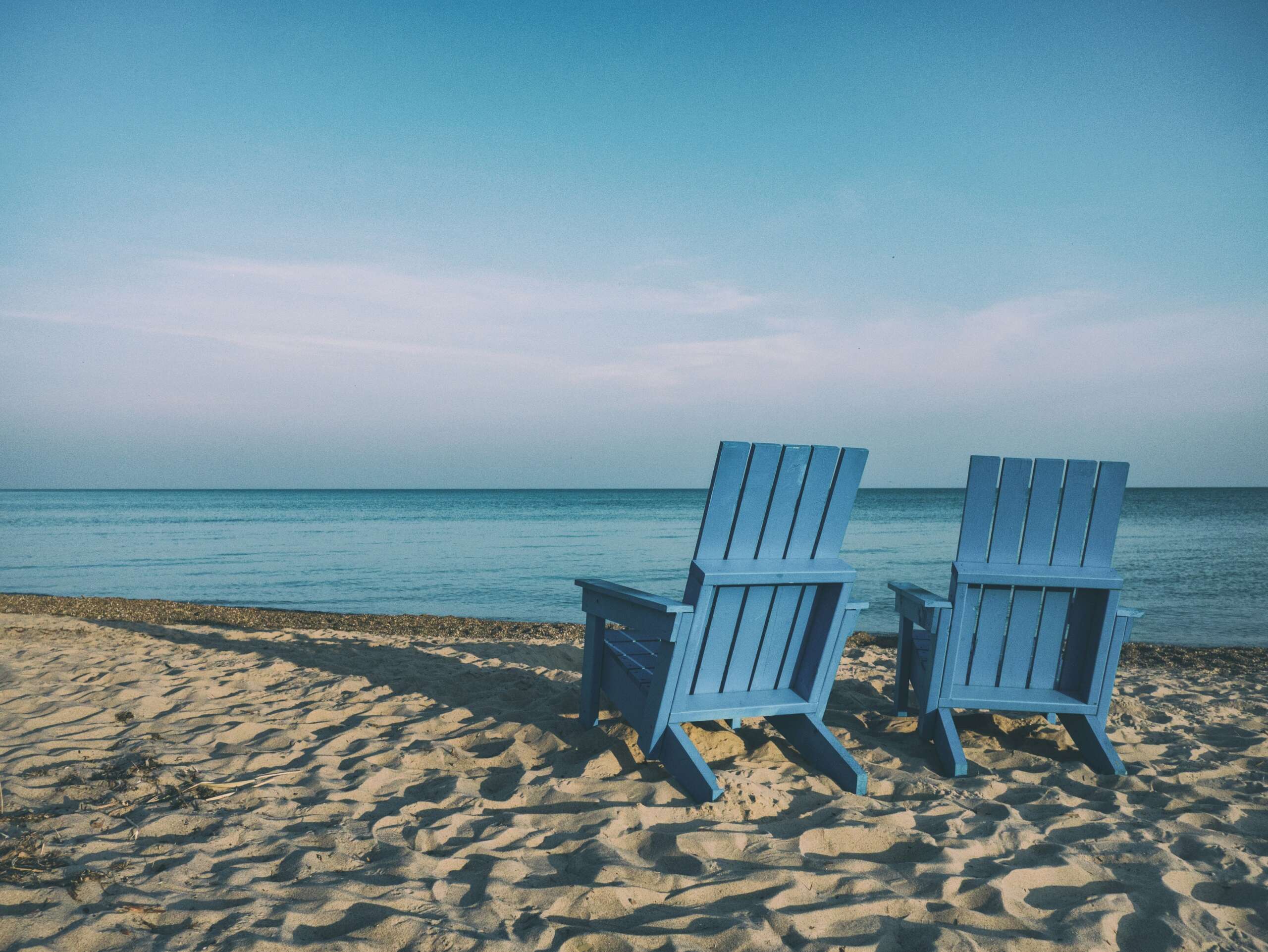 An image of two blue-colored beach chairs sitting in front of an ocean.