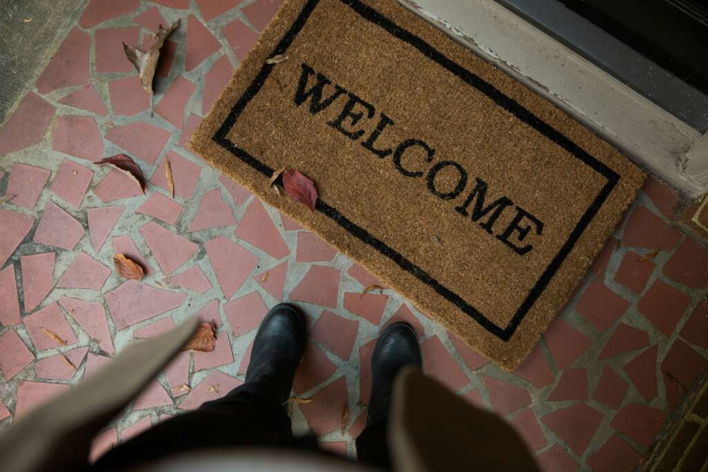 A person standing in front of a welcome mat outside of a home. 