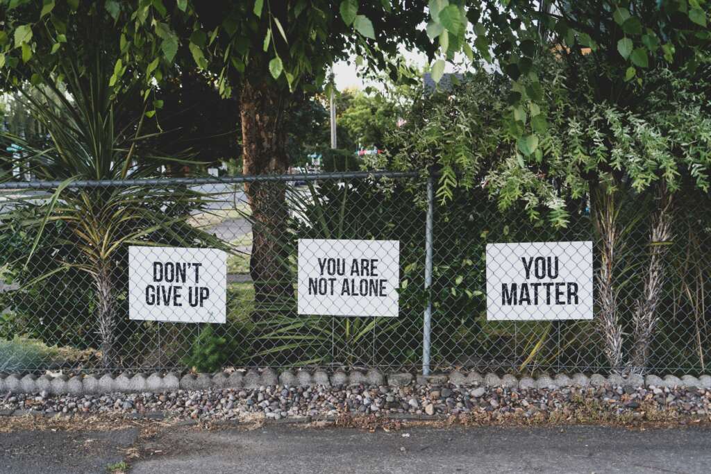A fence with a few different mental health awareness signs on it. 