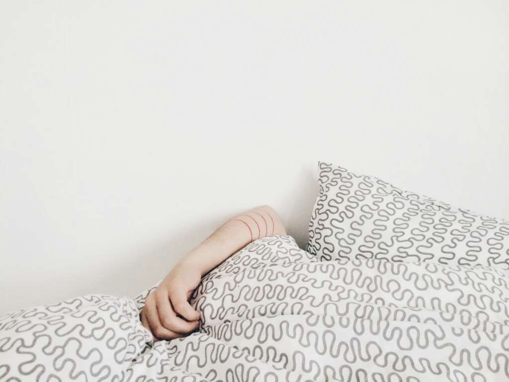 An image of a person sleeping underneath their covers with their arm showing. 