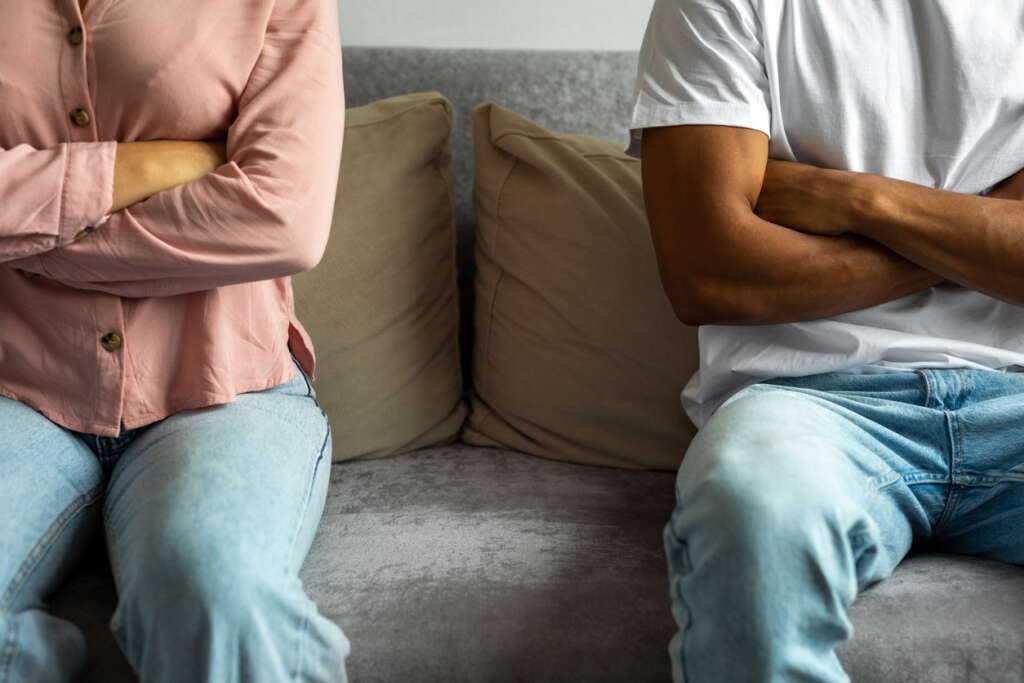 A couple seated next to each other on a couch with their arms crossed after being in an argument. 