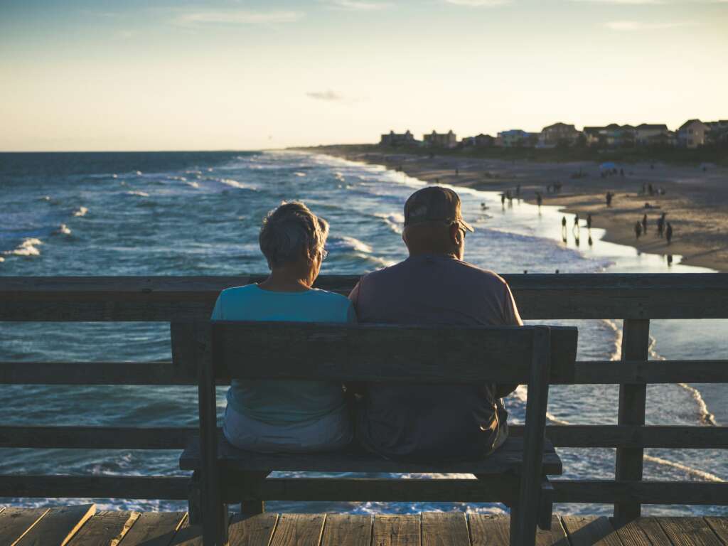 An older couple sitting next to each other while looking at the ocean.