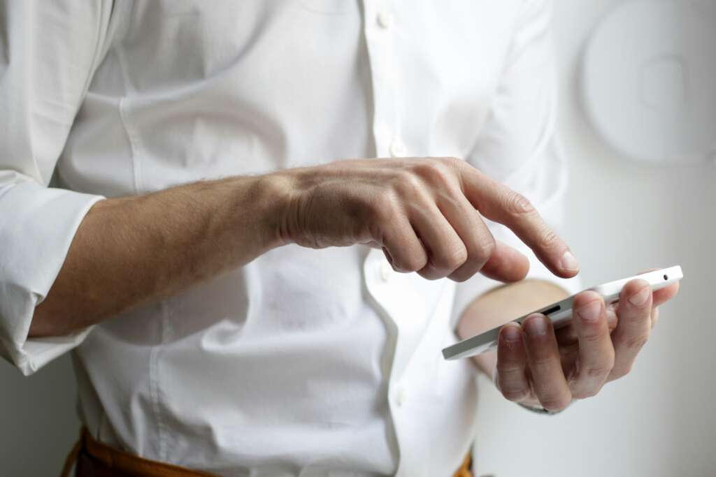 An image of a person in a white-collared shirt typing on their phone. 