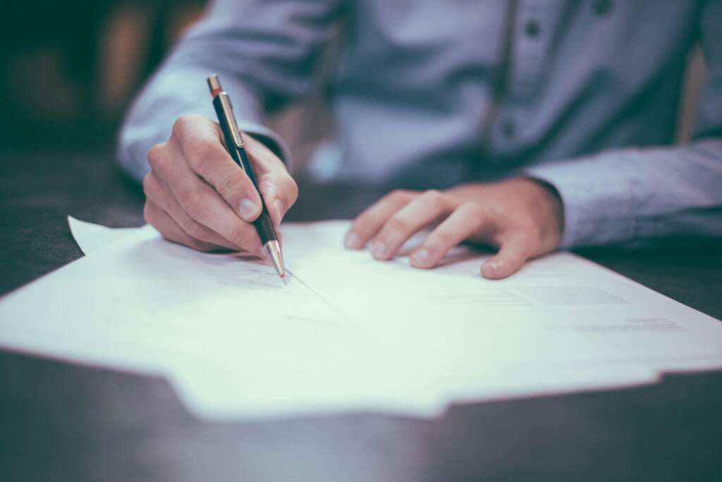 A close-up image of a person writing on paper that's been placed on a desk. 