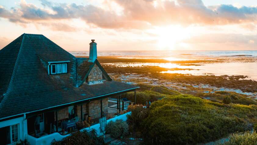 An image of a beautiful home located by the beach with a sunset in the background.