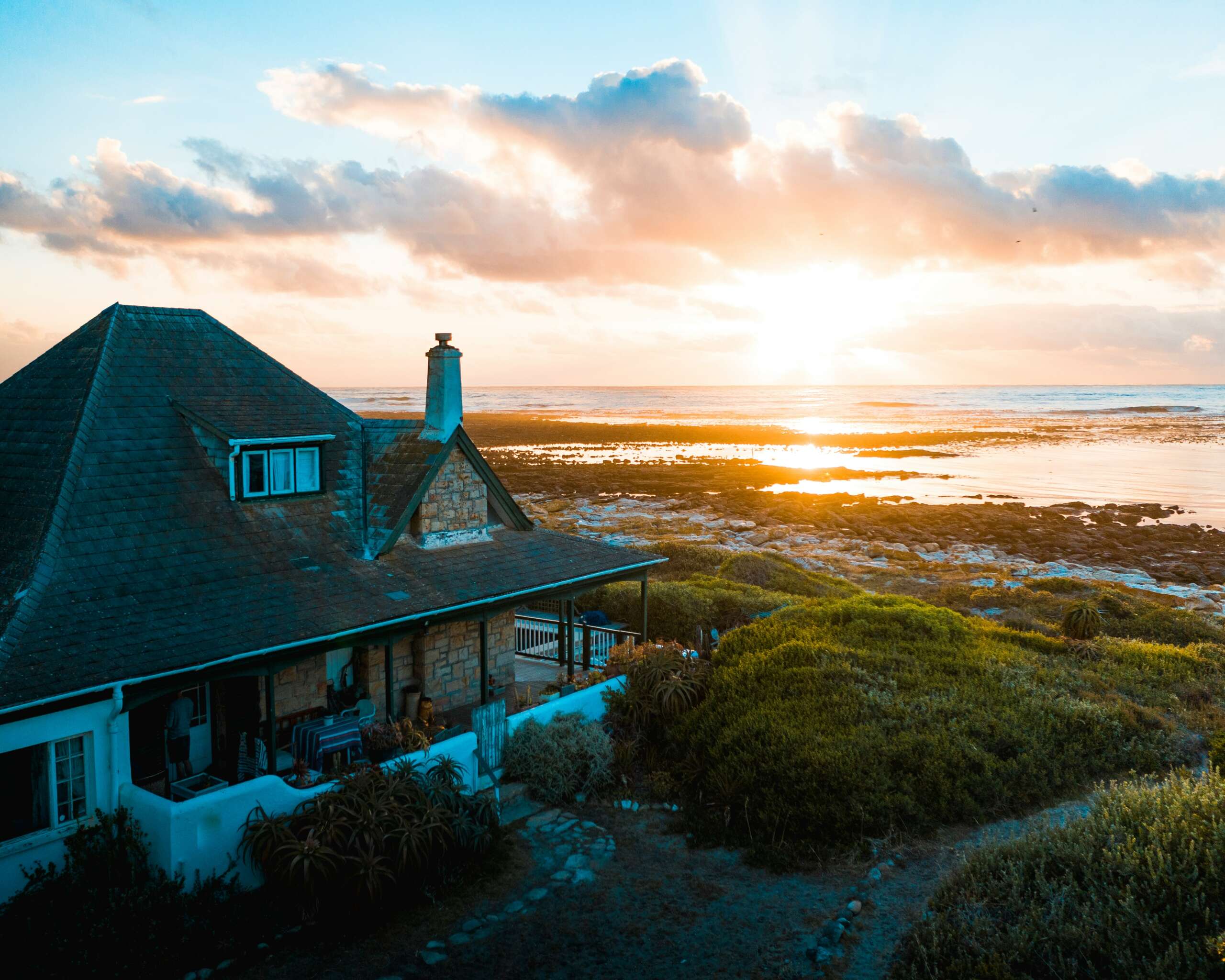 An image of a beautiful home located by the beach with a sunset in the background.