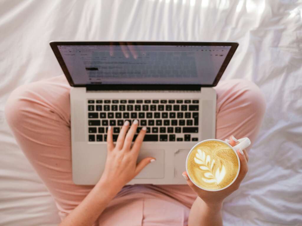 A person sitting in their bed with a cup of coffee in their hand. 
