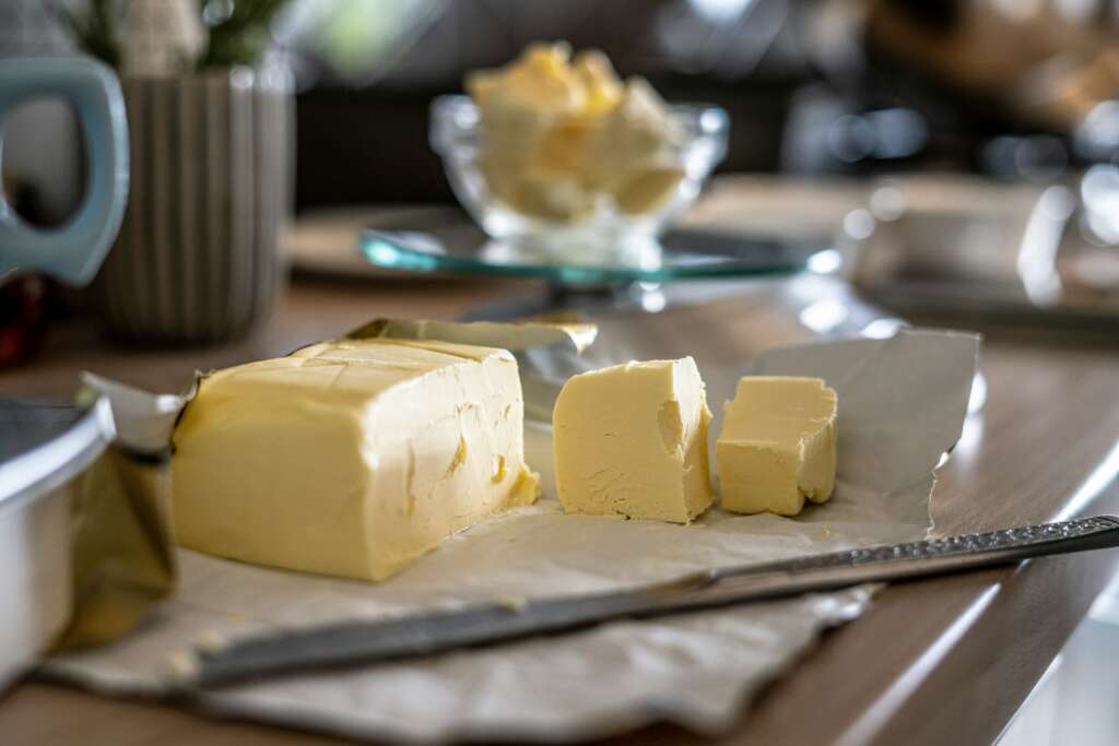 A stick of butter that's been placed on a countertop with a butter knife in front of it. 