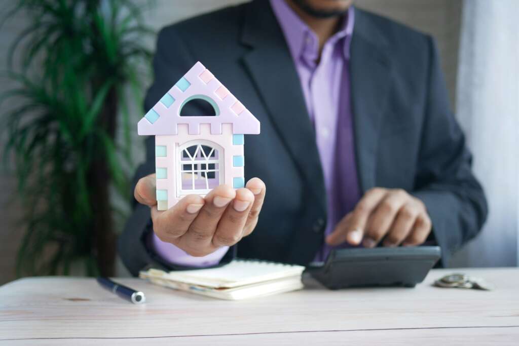 An image of a person in a suit holding up a model of a house to represent a housing loan. 