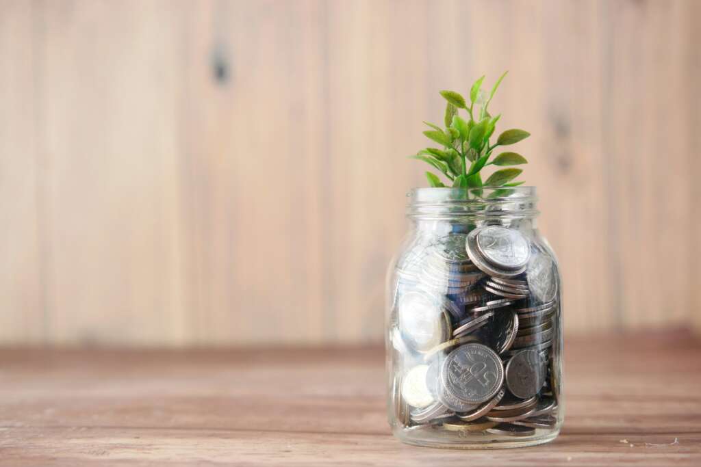 A jar of coins with a sprout coming out of it. 