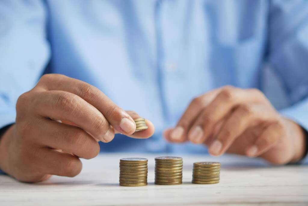 An image of a person in a blue button-down shirt stacking up gold-colored coins. 