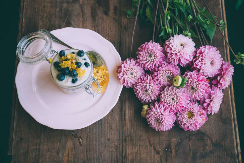 An image of sweetened yogurt placed next to pink flowers. 