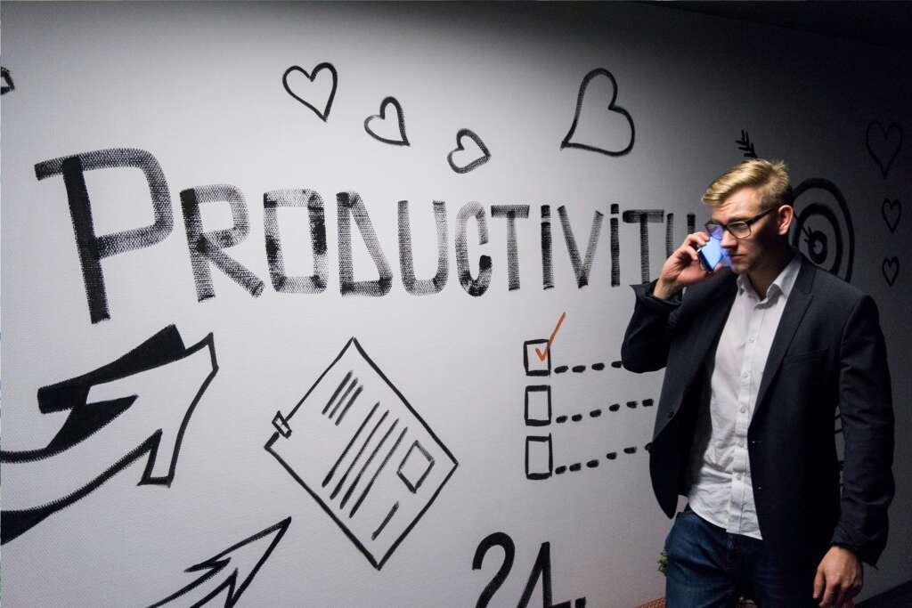 An image of a young man in glasses on the phone standing in front of a whiteboard that reads "productivity."