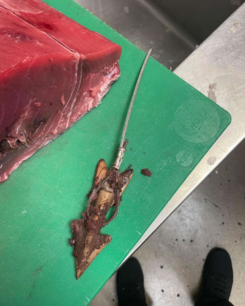 An image of a big slab of tuna on a green cutting board that's been placed next to a harpoon. 
