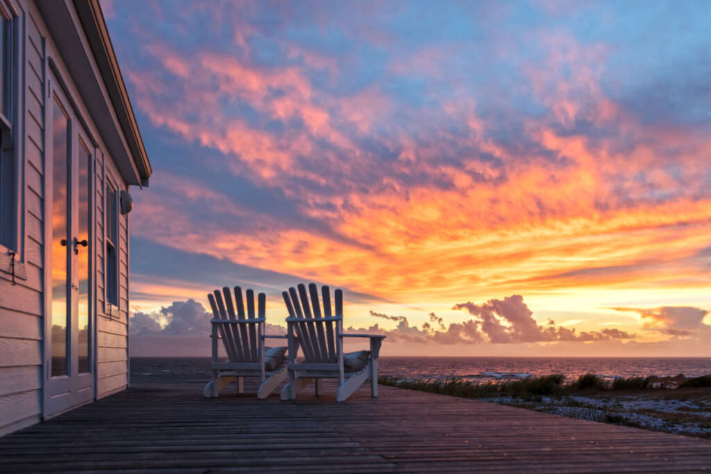 An image of two beach chairs set up in front of a sunset by the beach. 