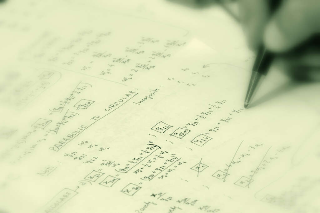 An image of a person using a pen to fill out calculus equations on a piece of paper. 