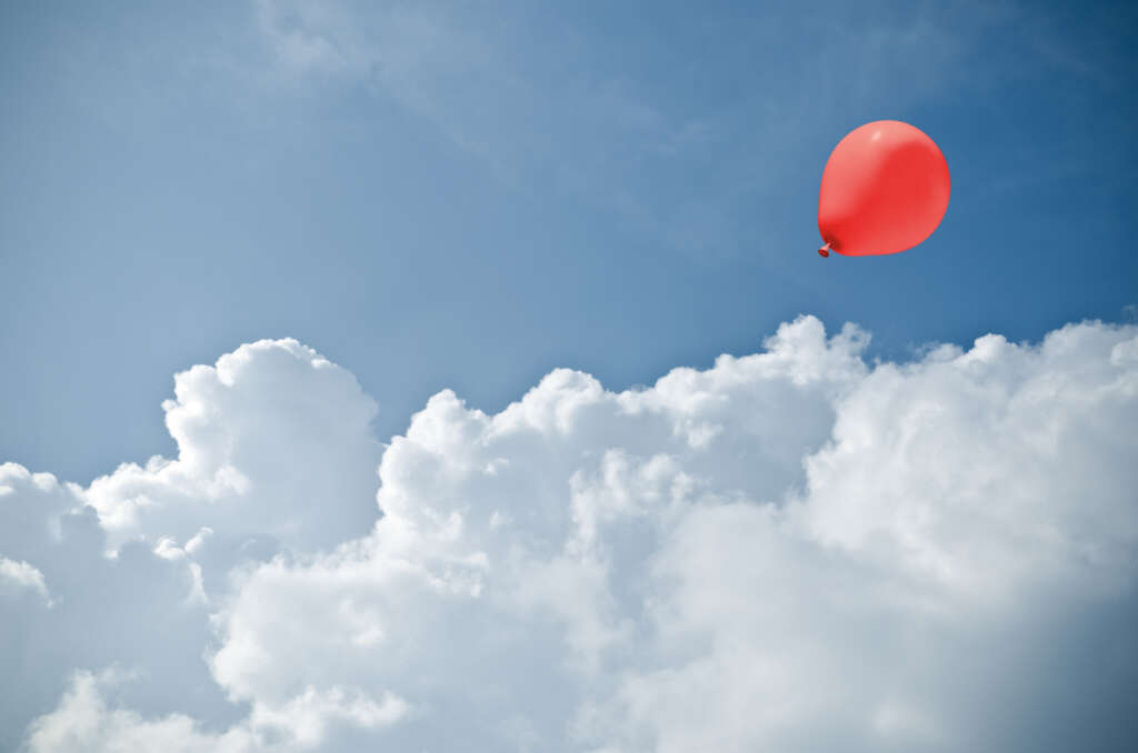 A red balloon floating away in a blue sky. 