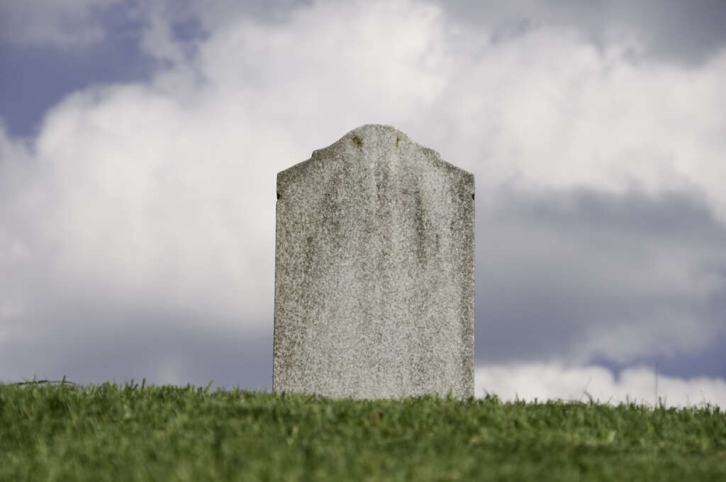 An image of a gravestone on a grassy hill. 