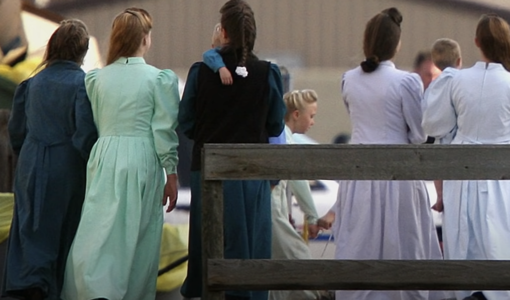 An image of women turned around while wearing old-fashioned dresses.  