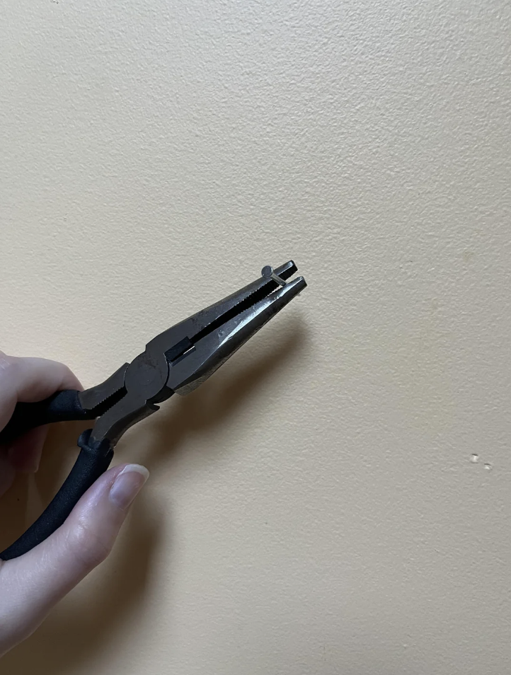 An image of someone using pliers to hold a small-sized nail in place. 