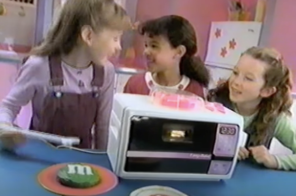 An image of an Easy-Bake Oven being played with by a few kids. 